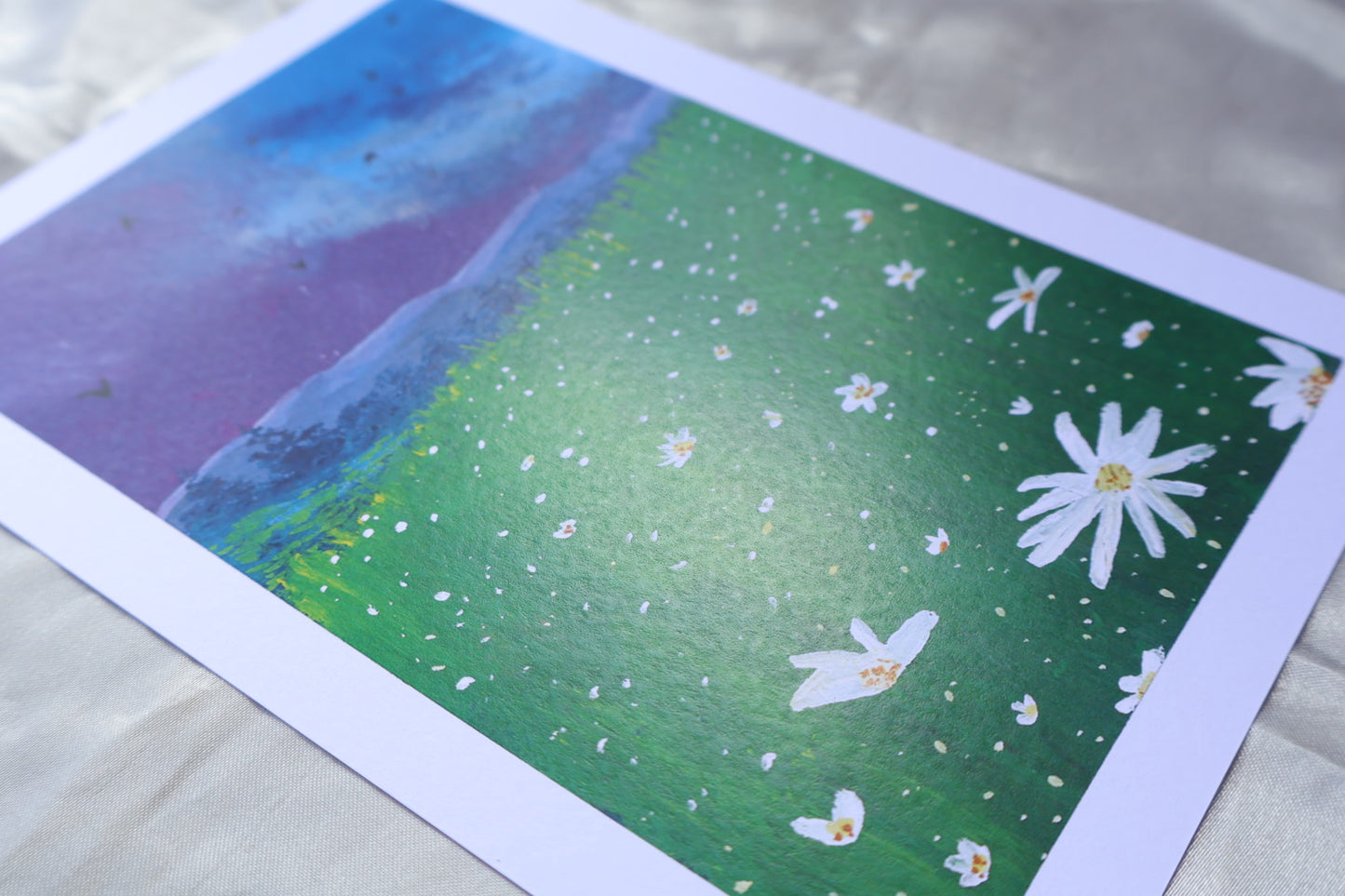 Purple bluey clouds under the dark evening blue sky, with soft mountains underneath it, covered with trees, followed by a bright foreground flowers, resembling daisies, glowing in the night sky, surrounded with yellowish and greenish tall grasses, meadow-like, and energetic birds flying in the sky.